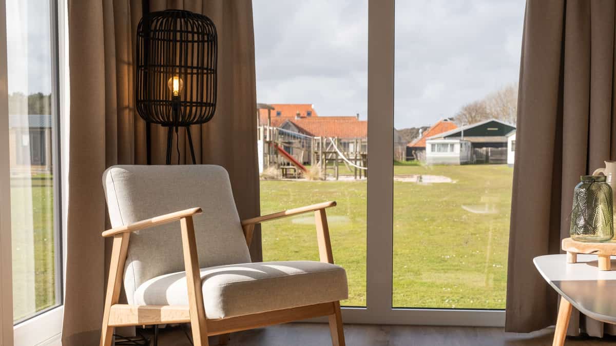 Zithoek met fauteuil en uitzicht op het veld in Chalet Deluxe Bonte Piet op Camping Cupido