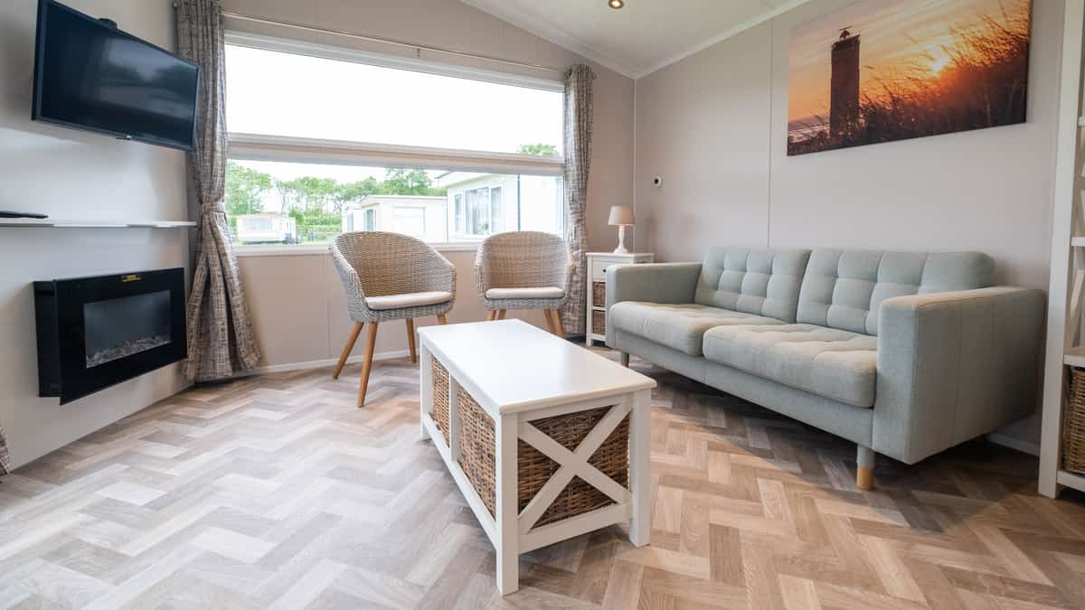 Woonkamer met grijze bank, rieten stoelen en wandtelevisie