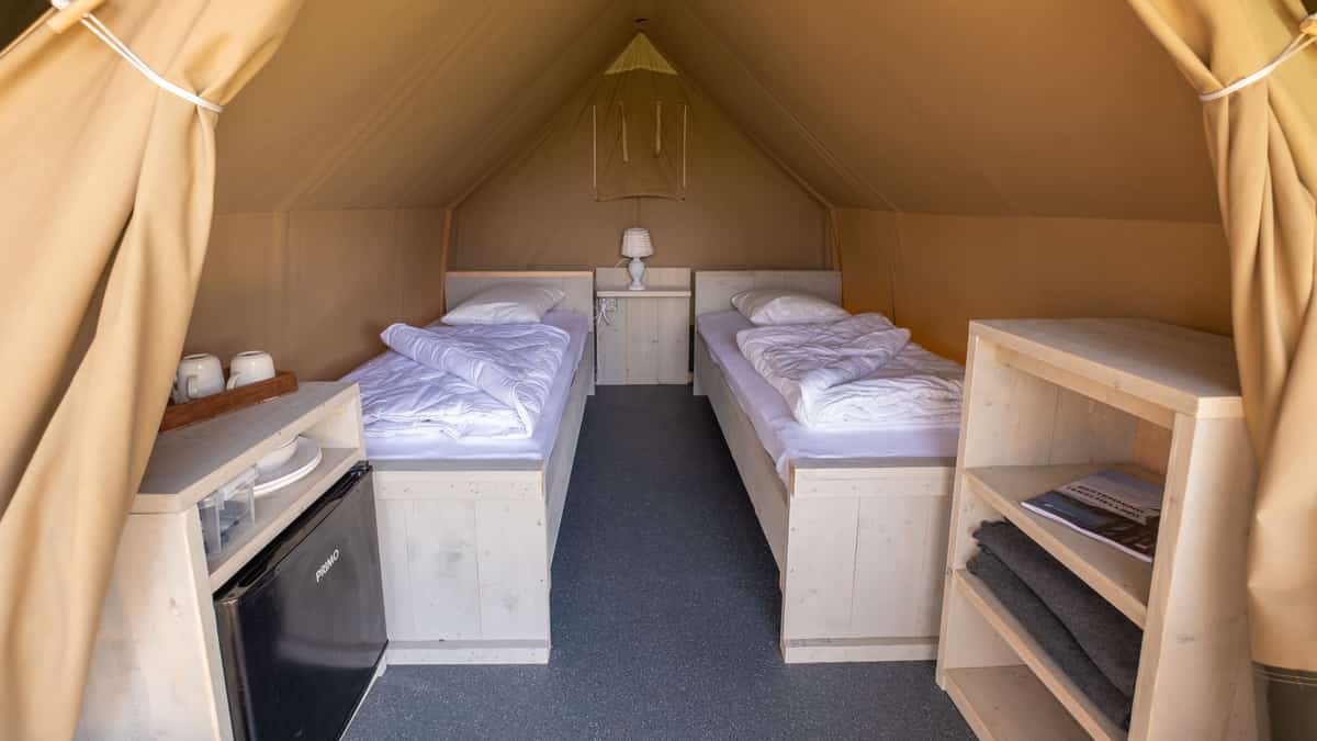 Twee eenpersoonsbedden met wit beddengoed in een beige tent