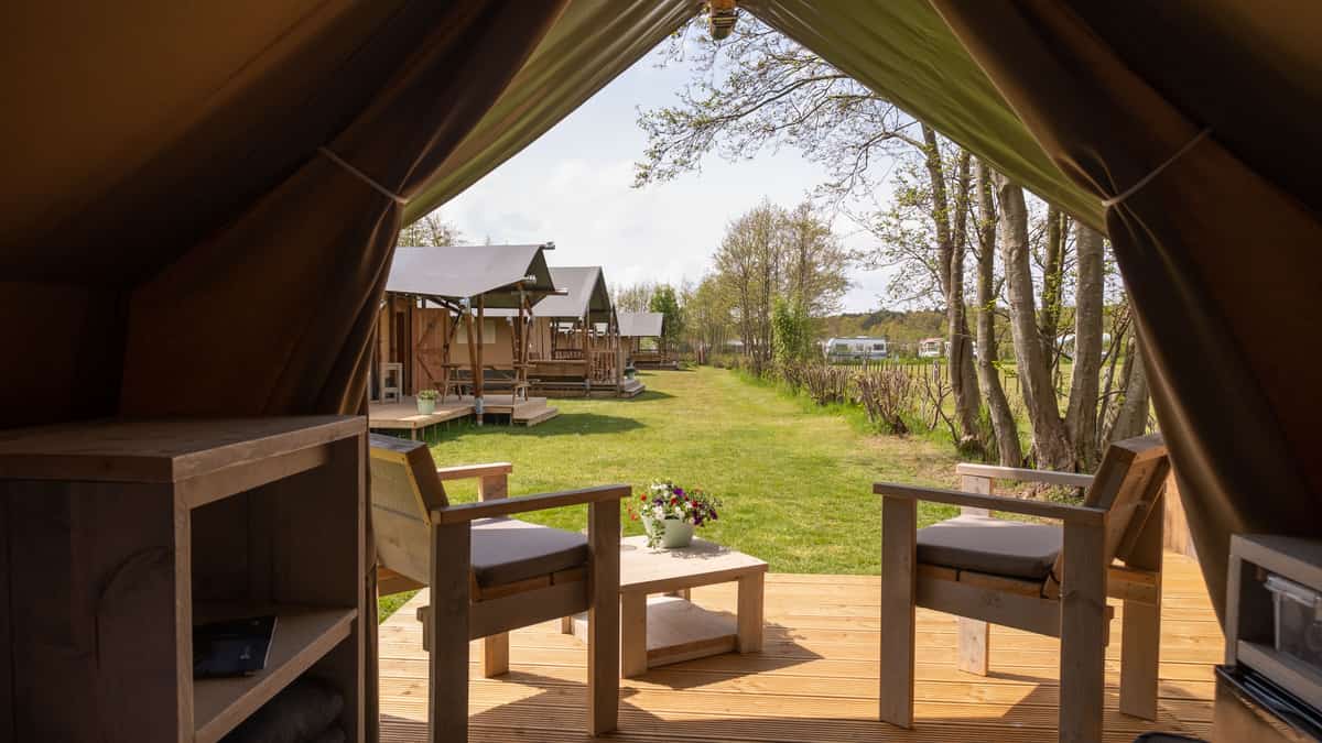 Houten terras met stoelen en uitzicht op safaritenten tussen bomen