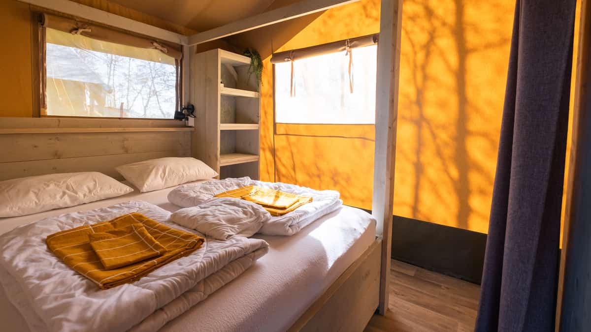Eenpersoonsbedden in houten slaapnissen met gordijnen en gele dekens