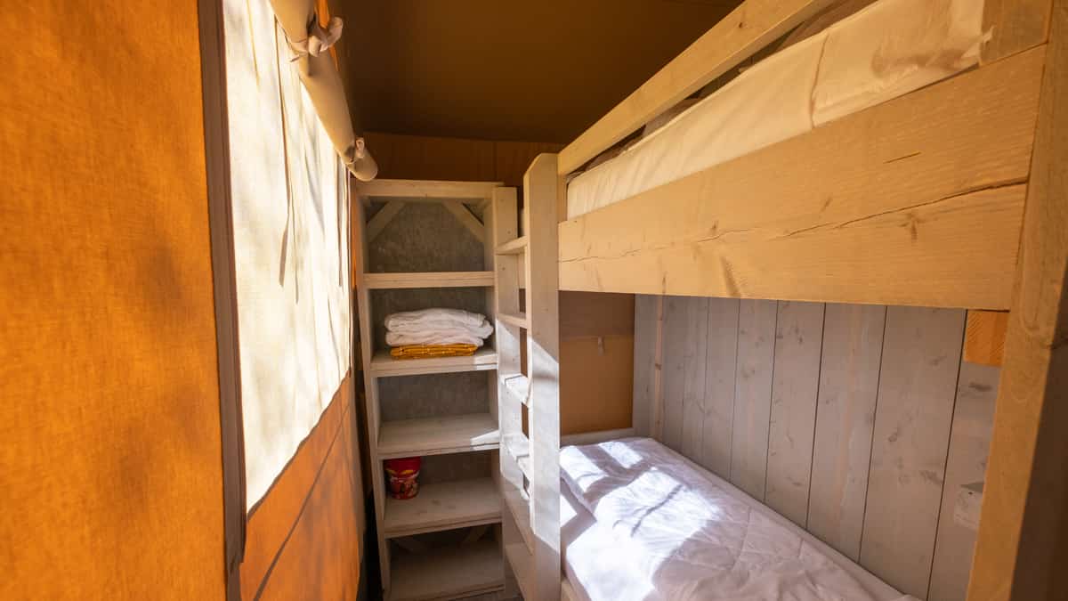 Houten stapelbedden met wit beddengoed naast een licht gordijn