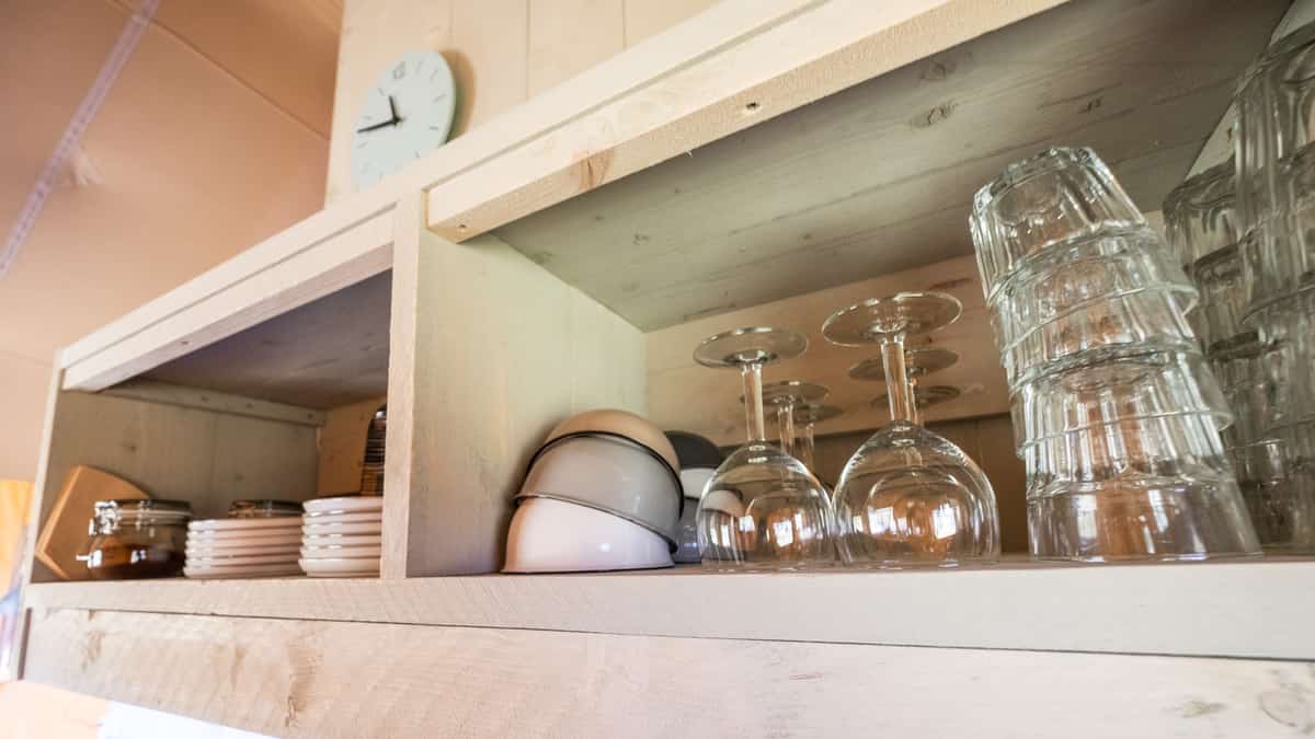 Gestapelde drinkglazen en witte kopjes op houten planken
