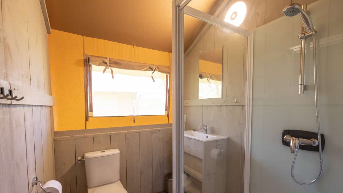 Badkamer met douche, toilet, wastafel en oranje rolgordijnen