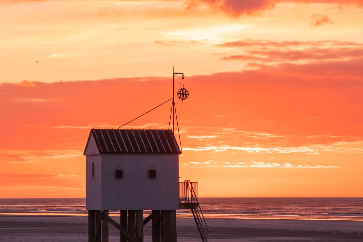 Strandhuisje op palen onder een oranje avondlucht op Terschelling