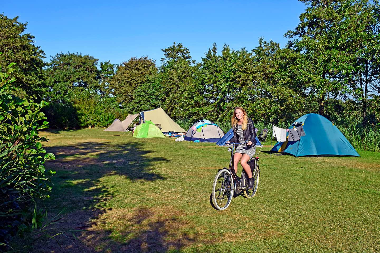 Vrouw fietst over grasveld langs tenten op een camping