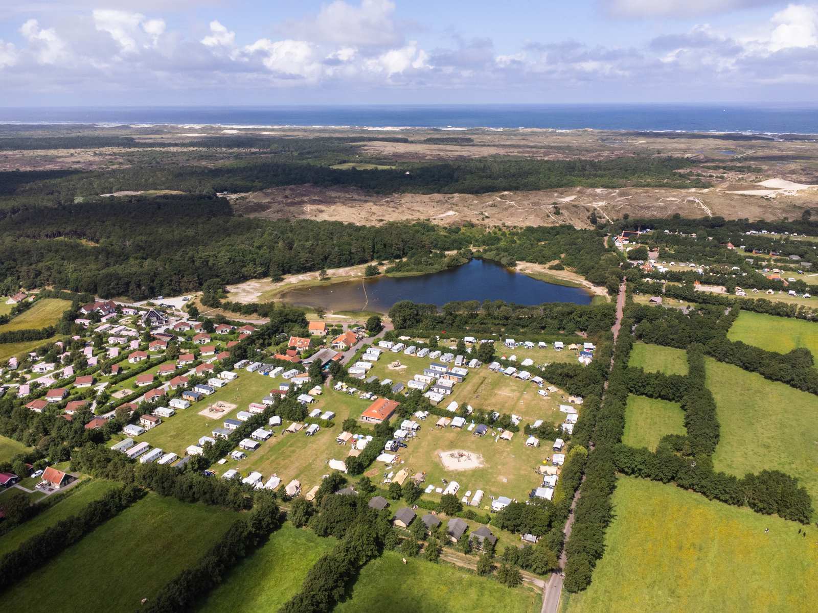 Luchtfoto van camping en vakantiehuisjes bij een meer, duinen en zee