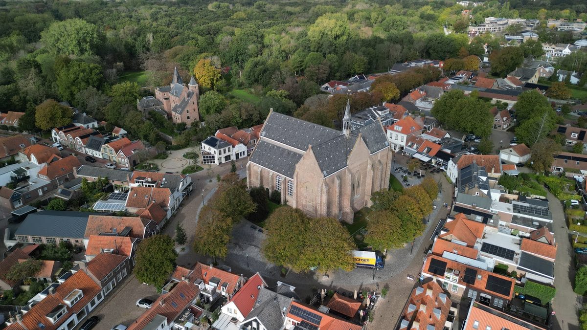 Luchtfoto van een kerk tussen dorpshuizen, met bos op de achtergrond