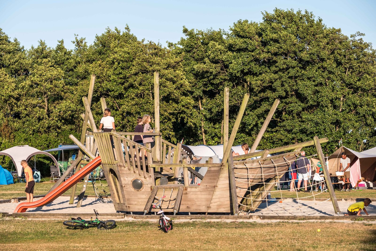 Kinderen bij houten speeltoestel met glijbaan en klimnet