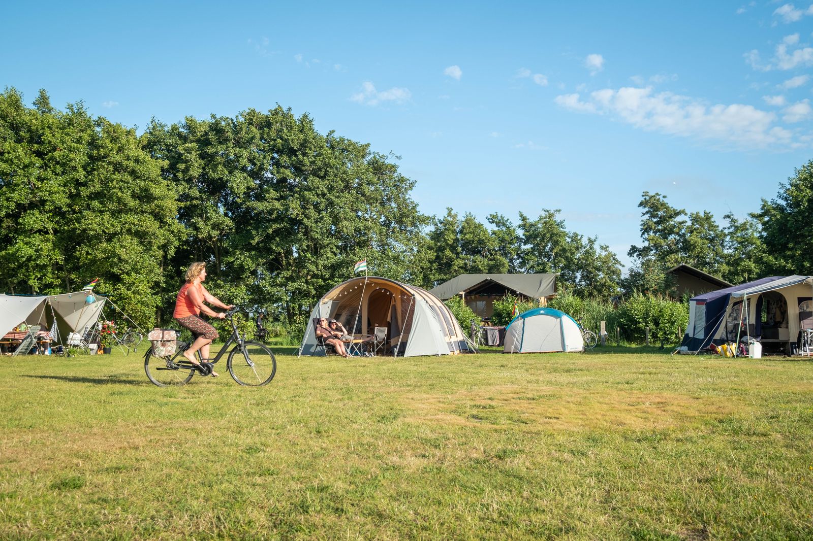 Vrouw fietst over gras langs tenten en bomen