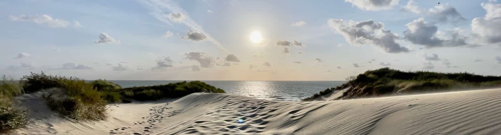 Voetsporen in zandduinen met uitzicht op zee en laagstaande zon