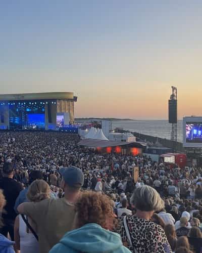Publiek bij een concert aan zee met podium en gestreepte vuurtoren