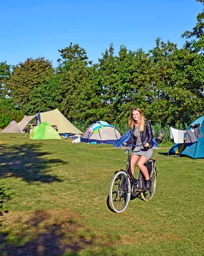 Vrouw fietst over grasveld langs tenten op een camping