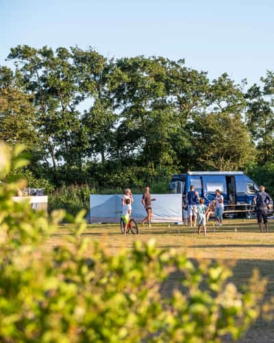 Kampeerders bij tenten en caravans aan de rand van een grasveld