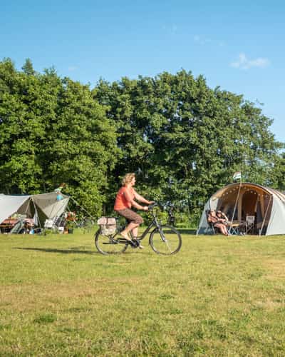 Vrouw fietst over gras langs tenten en bomen