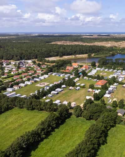 Luchtfoto van camping met tenten, stacaravans en meertje bij de duinen