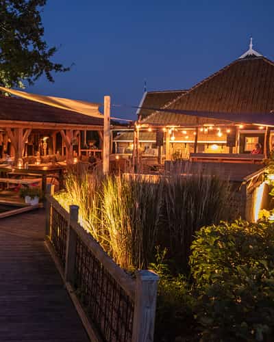 Houten vlonder langs een vijver naar verlicht terras bij schemering