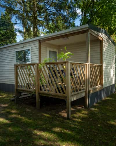 Mobilheim mit kleiner Holzveranda zwischen Bäumen