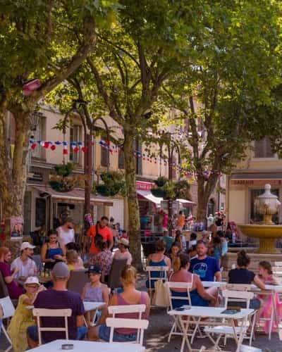 Mensen eten en drinken op straatcafés, met bomen en winkels eromheen