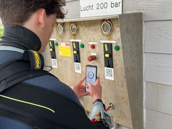 Duiker in duikpak gebruikt smartphone bij vulstation voor perslucht