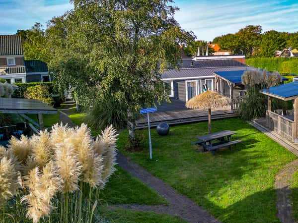 Groen grasveld met picknicktafel, rieten parasol en overdekt terras