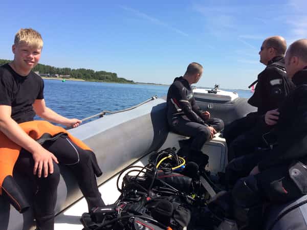 Vier mensen met duikuitrusting in een rubberboot op het water