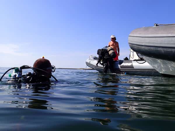 Duikers in het water naast twee rubberboten