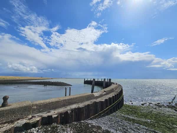Gebogen golfbreker aan zee onder een blauwe lucht met wolken