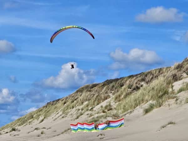 Paraglider boven grasduinen met kleurrijke windschermen op het zand