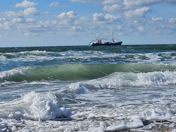 Vissersboot op zee achter schuimende golven