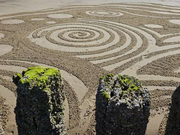 Spiraalpatronen in strandzand met begroeide strandpalen op de voorgrond