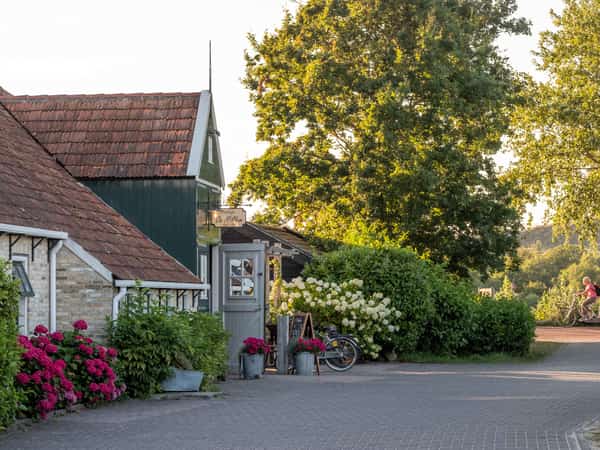 Twee fietsers bij een gebouw met rood pannendak en bloeiende hortensia’s