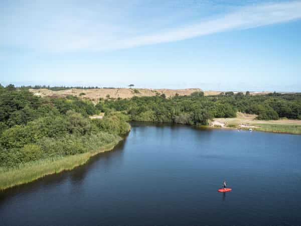 Peddelaar op rood paddleboard op meer met duinen en bomen
