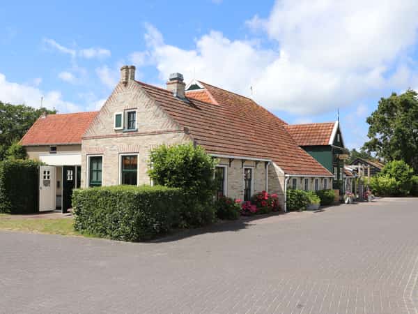 Bakstenen huizen met pannendaken, groene luiken en heggen langs een klinkerweg