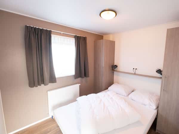 Slaapkamer met twee eenpersoonsbedden, grijze gordijnen en houten kast