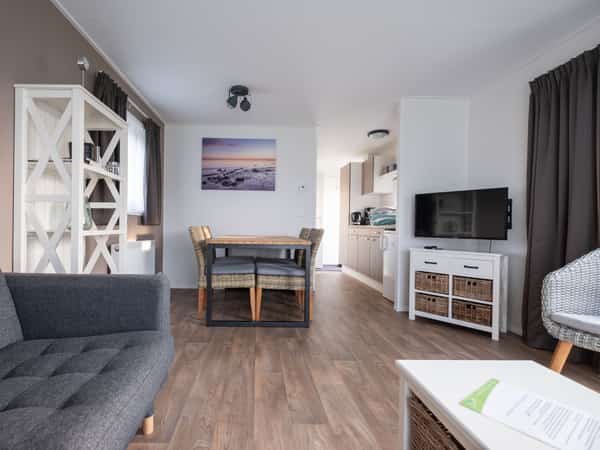 Woonkamer met grijze bank, televisie, eettafel en open keuken