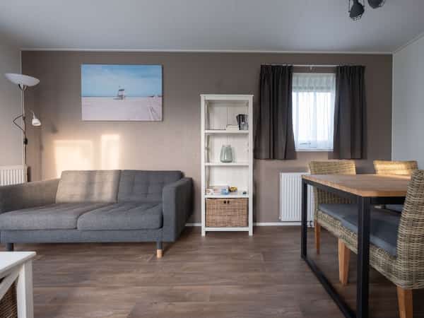 Woonkamer met grijze bank, rotan stoelen en strandfoto aan de muur
