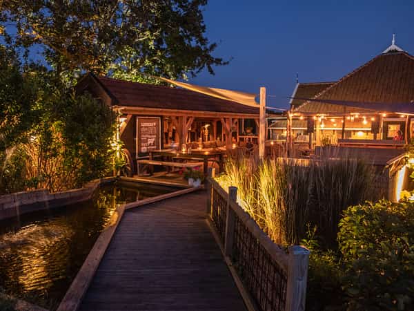 Houten vlonder langs een vijver naar verlicht terras bij schemering