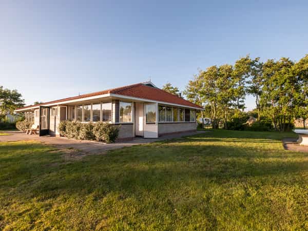 Vakantiehuis met rood pannendak tussen bomen en grasvelden