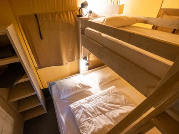 Rijen stapelbedden met beige beddengoed en leeslampjes