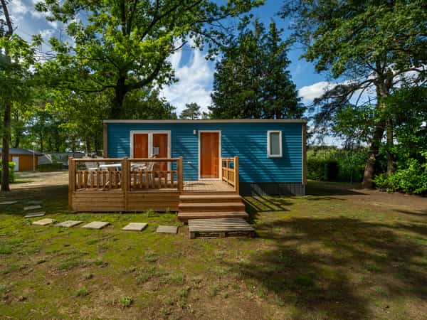 Blauw vakantiehuisje met houten terras in een groene tuin