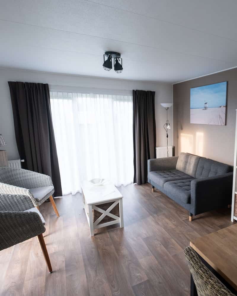 Woonkamer met rieten stoelen, witte tafel en grijze bank