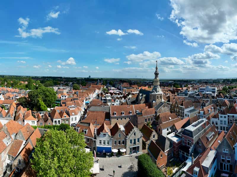 Uitzicht over rode daken, kerktorens en water onder een wolkenlucht