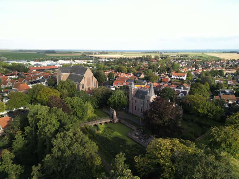 Luchtbeeld van kasteel en kerk tussen bomen en dorpshuizen