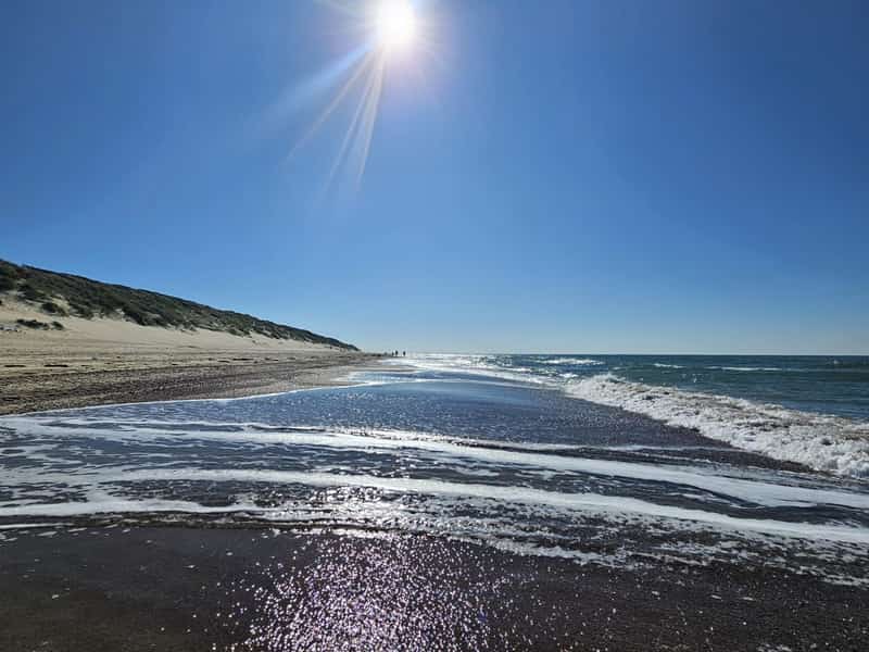 Zon boven een zandstrand met duinen en golven
