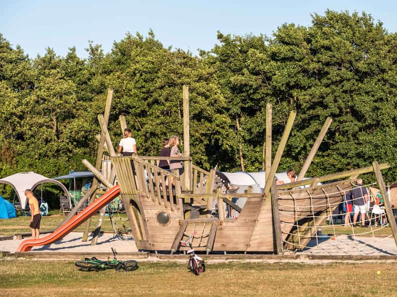 Kinderen bij houten speeltoestel met glijbaan en klimnet