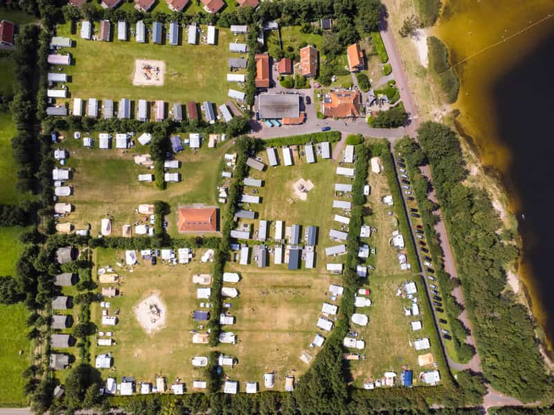 Luchtfoto van een camping met caravans, tenten en een meer