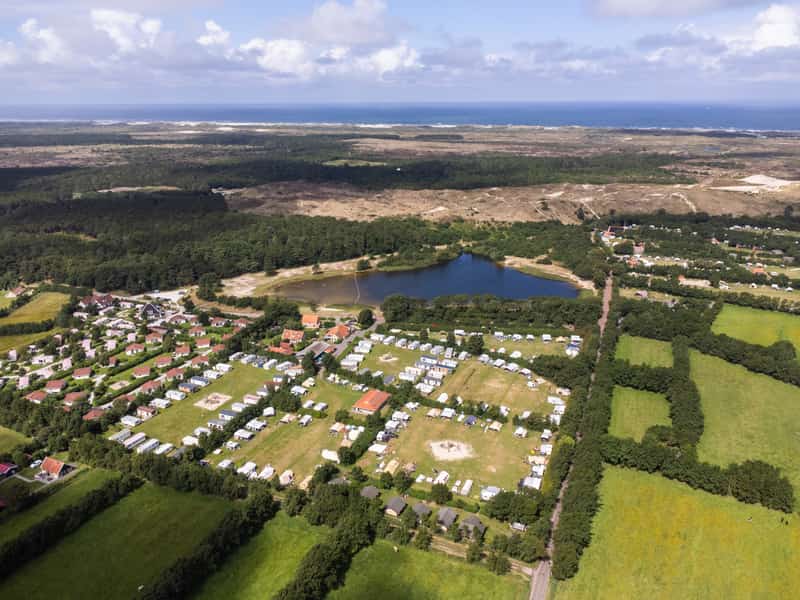 Luchtfoto van camping en vakantiehuisjes bij een meer, duinen en zee